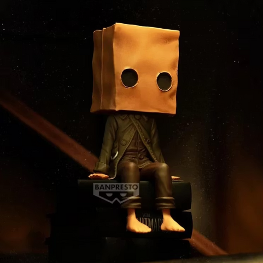 Figurine Mono Monitor Top Figure Vol. 2 – Little Nightmares II, assis sur une pile de livres avec son sac en papier.