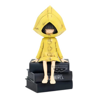Figurine Six Monitor Top Figure Vol. 1 – Little Nightmares, assise sur une pile de livres noirs avec son imperméable jaune.