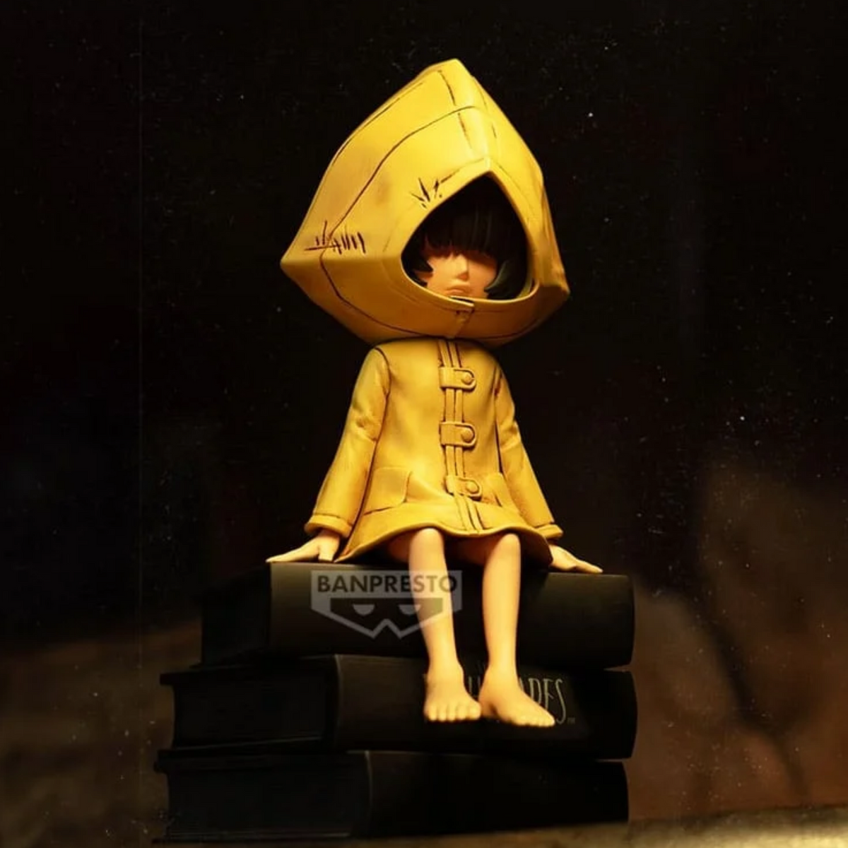 Figurine Six Monitor Top Figure Vol. 1 – Little Nightmares, assise sur une pile de livres noirs en imperméable jaune.