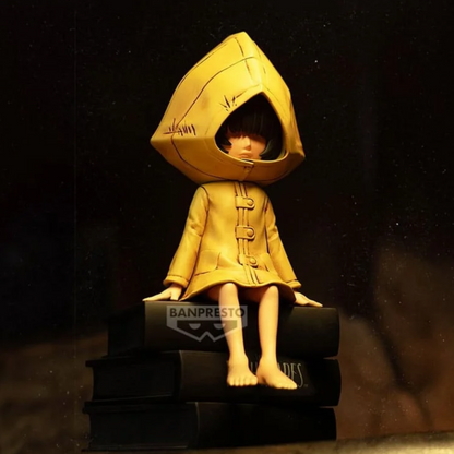 Figurine Six Monitor Top Figure Vol. 1 – Little Nightmares, assise sur une pile de livres noirs en imperméable jaune.